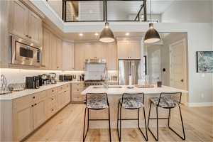 Kitchen with a kitchen island with sink, a kitchen breakfast bar, a high ceiling, light hardwood / wood-style flooring, and stainless steel appliances