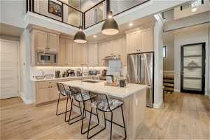 Kitchen with a high ceiling, a center island with sink, appliances with stainless steel finishes, light hardwood / wood-style flooring, and a breakfast bar area