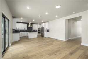 Kitchen featuring white cabinets, wall chimney range hood, backsplash, and light wood-type flooring