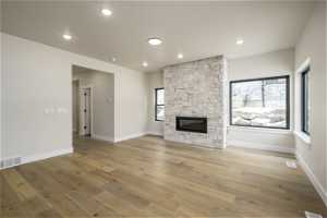 Unfurnished living room with a stone fireplace, a wealth of natural light, and light hardwood / wood-style flooring