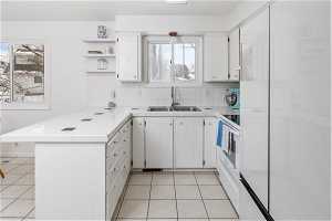 Kitchen featuring tile counters, light tile floors, sink, tasteful backsplash, and white cabinetry