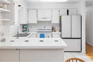 Kitchen featuring tile countertops, sink, white appliances, and kitchen peninsula