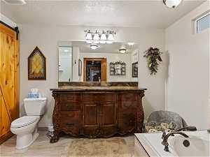 Bathroom with a tub, a textured ceiling, large vanity, toilet, and tile flooring