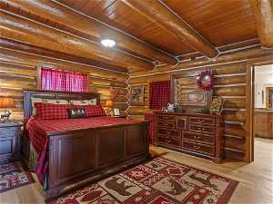 Bedroom featuring light hardwood / wood-style flooring, beamed ceiling, wood ceiling, and rustic walls