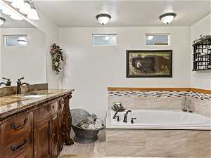 Bathroom featuring vanity, a textured ceiling, and tiled tub