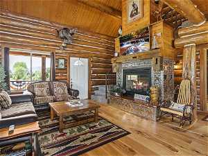 Living room with light hardwood / wood-style floors, log walls, wood ceiling, beam ceiling, and high vaulted ceiling