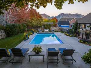 Pool at dusk with a yard, a patio, and a mountain view, and rock wall fence
