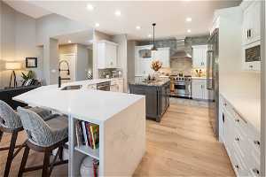 Kitchen with tasteful backsplash, wall chimney exhaust hood, white cabinetry, high end appliances, and a center island