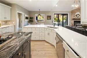 Kitchen featuring decorative light fixtures, dishwasher, white cabinets, a large fireplace, and sink