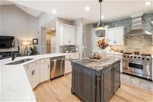 Kitchen featuring a kitchen island, wall chimney exhaust hood, backsplash, white cabinets, and stainless steel appliances