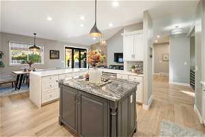 Kitchen featuring a kitchen island, lofted ceiling, white cabinetry, backsplash, and light hardwood / wood-style flooring