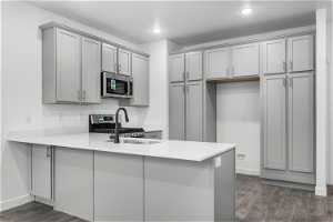 Kitchen featuring dark hardwood / wood-style flooring, kitchen peninsula, stainless steel appliances, and gray cabinets