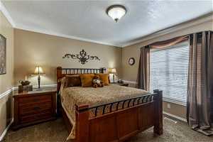 Guest bedroom with queen bed and dressers. Carpeted bedroom featuring crown molding and a textured ceiling