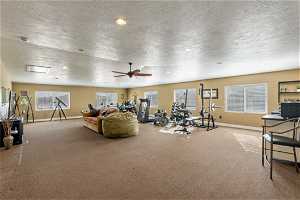 Exercise area with a textured ceiling, light carpet, and ceiling fan