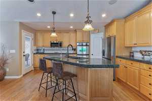 Kitchen featuring a kitchen bar, hanging light fixtures, appliances with stainless steel finishes, light hardwood / wood-style flooring, and a center island with sink