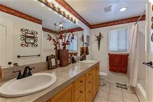 Main bathroom featuring a textured ceiling, oversized vanity, dual sinks, tile floors, combined shower/ tub and toilet