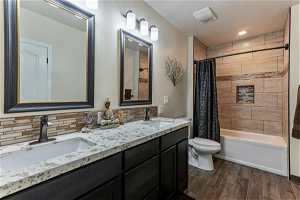 Full bathroom with shower / bath combo with shower curtain, large vanity, double sink, toilet, and tile floors