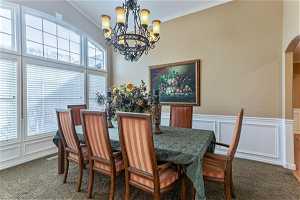 Dining area with crown molding, dark carpet, a notable chandelier, and a healthy amount of sunlight