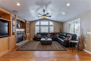 Living room featuring a stone fireplace, vaulted ceiling, hardwood flooring, ceiling fan, custom built-ins.