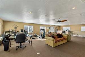 Living room with a textured ceiling, dark colored carpet, and ceiling fan