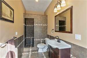 Bathroom featuring vanity, a tile shower, tile walls, tile floors, and toilet