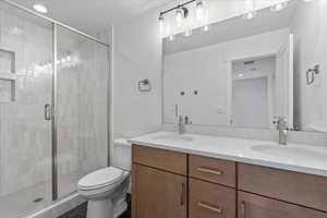 Bathroom with toilet, double sink vanity, and a shower with door