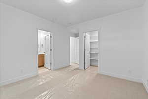 Unfurnished bedroom with a closet, ensuite bathroom, light colored carpet, and a walk in closet