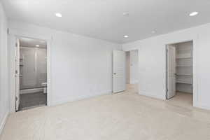 Unfurnished bedroom featuring a spacious closet, a closet, connected bathroom, and light colored carpet