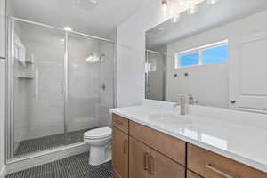 Bathroom featuring a shower with door, vanity, tile patterned floors, and toilet