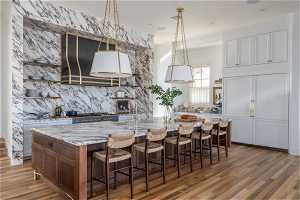 Kitchen with a kitchen breakfast bar, light stone countertops, hanging light fixtures, a center island with sink, and hardwood / wood-style flooring