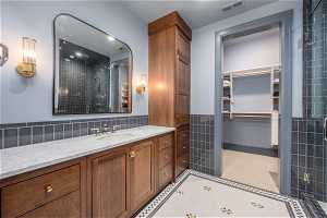 Bathroom with large vanity, tile walls, tile floors, backsplash, and a shower with door