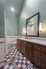 Bathroom with toilet, vanity, vaulted ceiling, tile walls, and tile flooring