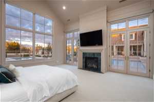 Bedroom featuring french doors, a tiled fireplace, access to exterior, high vaulted ceiling, and light carpet