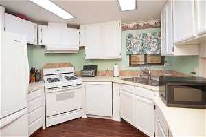Kitchen featuring dark wood-type flooring, white cabinets, range hood, and white appliances