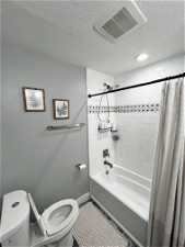 Bathroom with shower / bath combination with curtain, toilet, and a textured ceiling