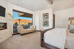 Carpeted bedroom with a high end fireplace and ceiling fan