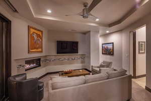 Living room featuring a tray ceiling, light tile floors, and ceiling fan