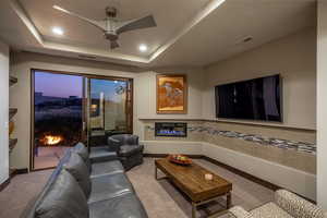 Carpeted living room with ceiling fan and a raised ceiling