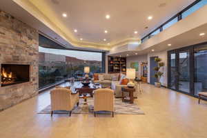 Living room featuring a stone fireplace, light tile flooring, and a high ceiling