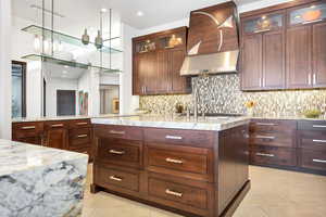 Kitchen featuring light tile flooring, wall chimney range hood, light stone countertops, and hanging light fixtures