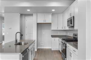 Kitchen featuring appliances with stainless steel finishes, white cabinets, sink, light hardwood / wood-style floors, and a kitchen island with sink