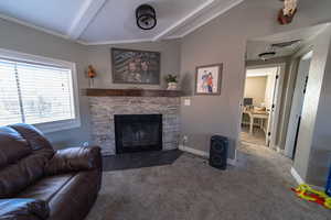 Living room featuring a stone fireplace, vaulted ceiling with beams, and dark carpet