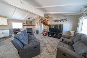 Tiled living room featuring a stone fireplace, vaulted ceiling with beams, and a healthy amount of sunlight