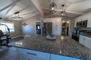 Kitchen featuring hanging light fixtures, appliances with stainless steel finishes, tile floors, a kitchen island, and white cabinetry