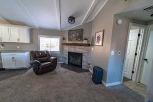 Carpeted living room featuring lofted ceiling with beams and a stone fireplace