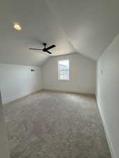 Additional living space with light carpet, baseboards, visible vents, lofted ceiling, and ceiling fan