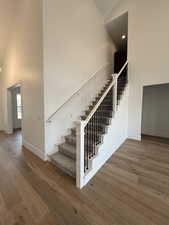 Stairway with baseboards, wood finished floors, and high vaulted ceiling