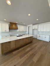 Kitchen with a textured ceiling, light wood finished floors, premium range hood, white cabinets, and recessed lighting