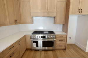Kitchen featuring range with two ovens, light wood-style floors, light brown cabinetry, and tasteful backsplash