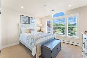 Bedroom featuring a baseboard heating unit, light colored carpet, and multiple windows